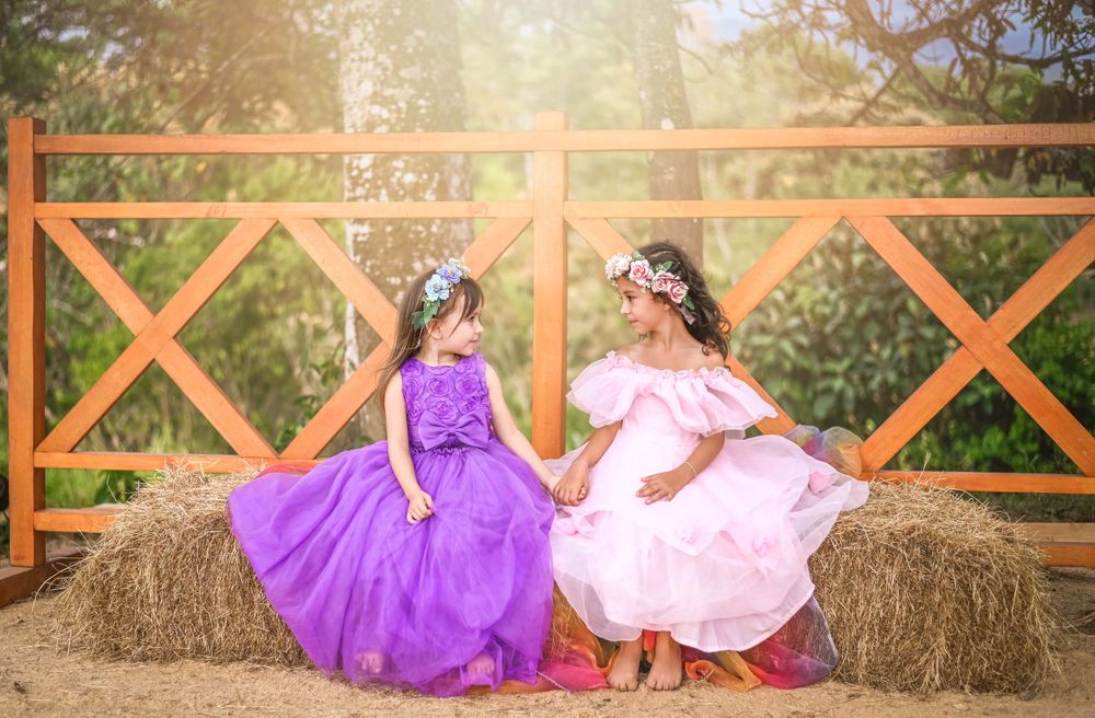 Two elegant dresses in pink and purple sitting on hay bales against a rustic wooden fence.