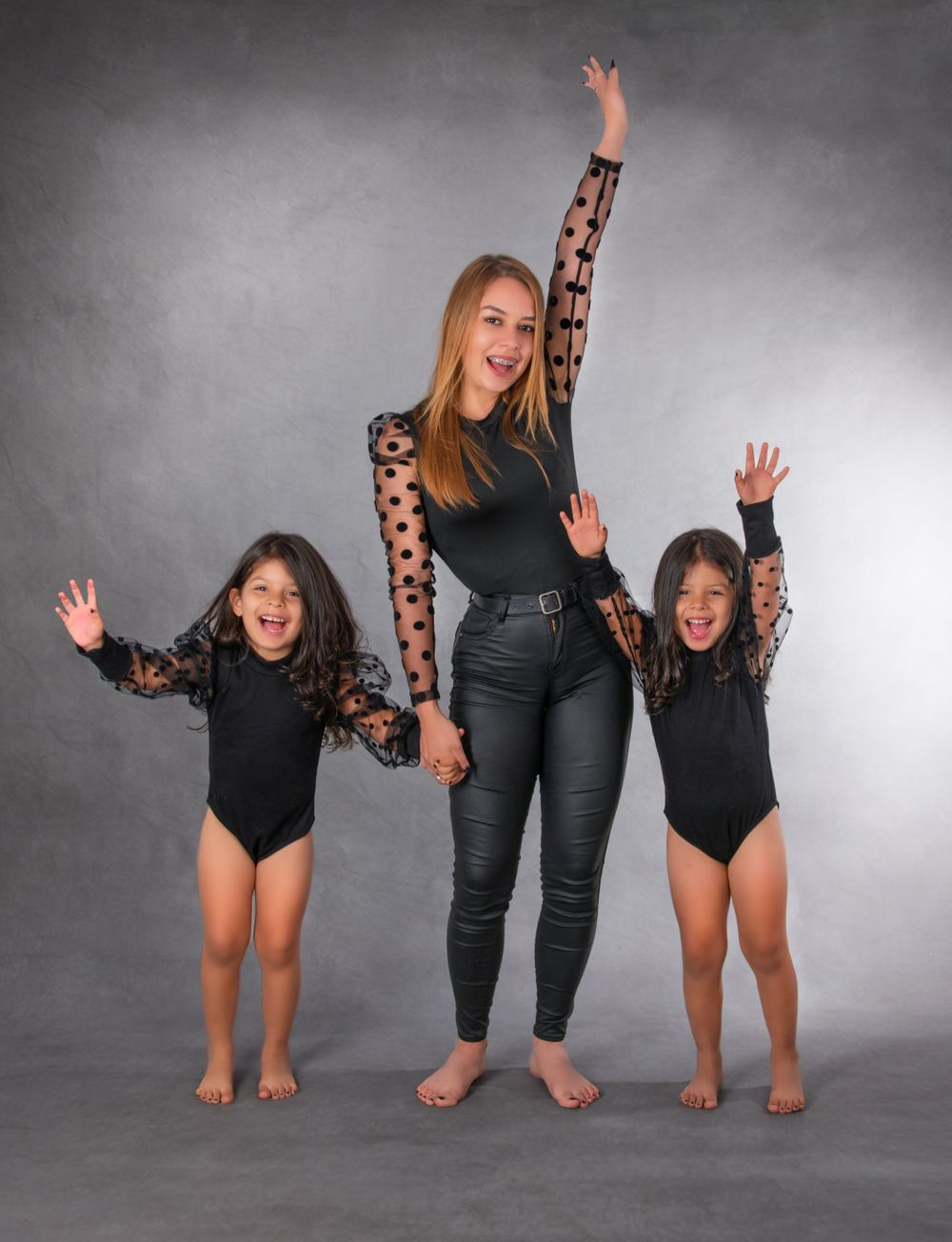 Three people in matching black outfits strike energetic poses against a grey studio background.