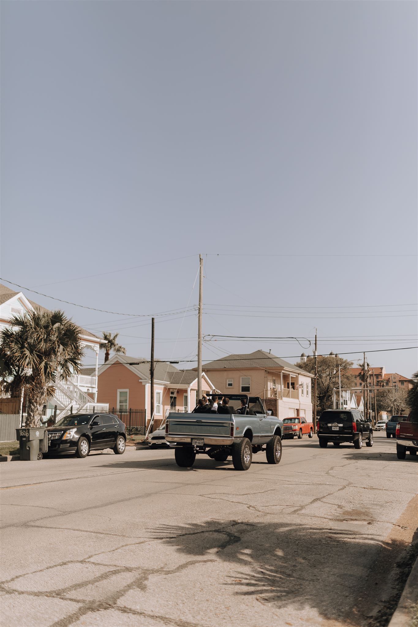 Three lifted trucks parked on a sunny residential street with palm trees and power lines.