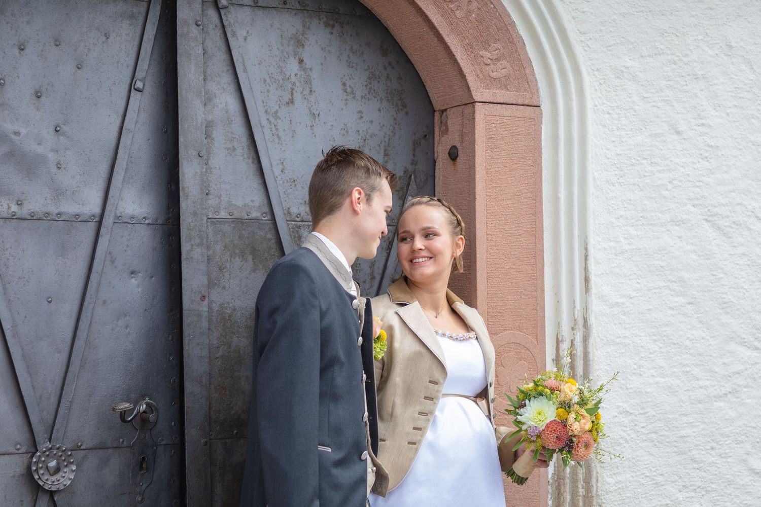 Romantic wedding photo of couple in arched doorway with bridal bouquet.