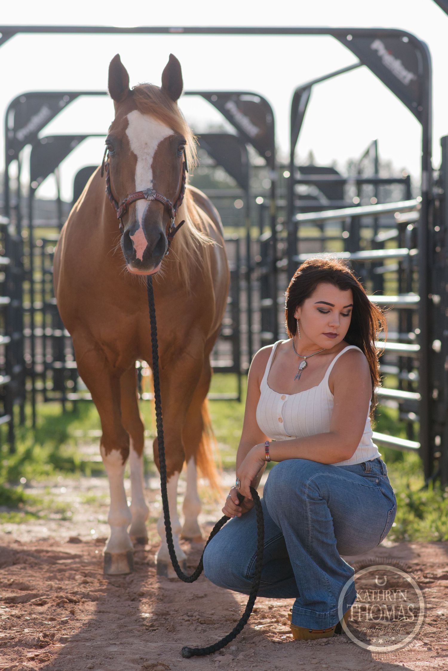 A chestnut horse with white blaze stands near metal gates in an outdoor ranch setting.