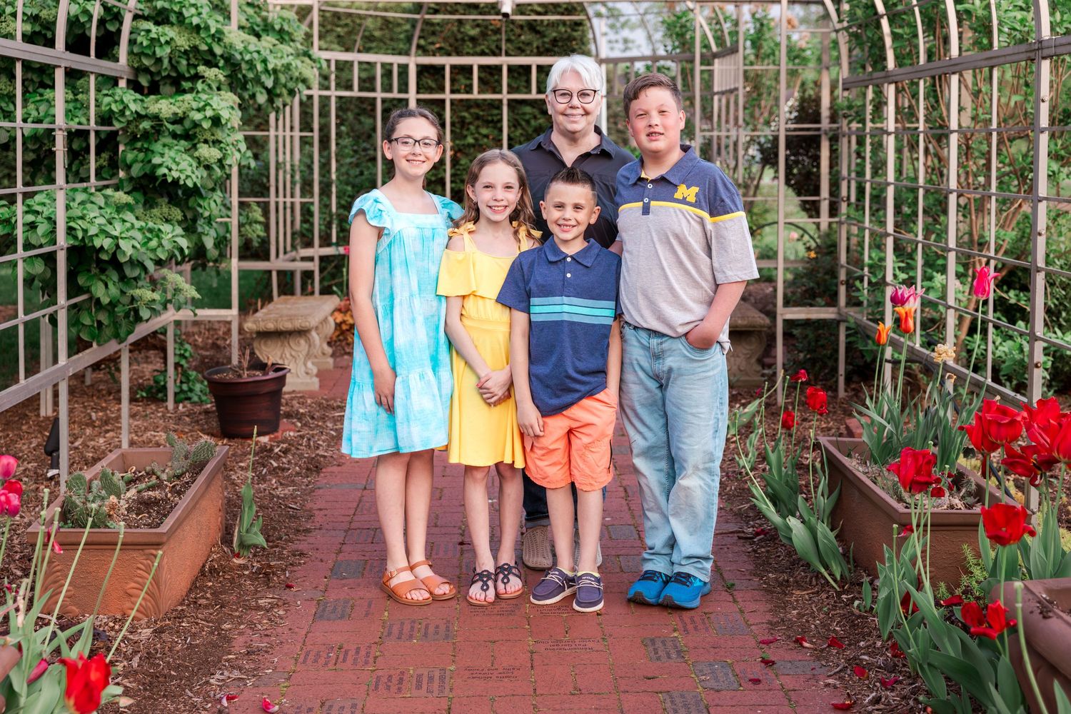 Group portrait in a garden archway with red tulips blooming along the brick pathway.