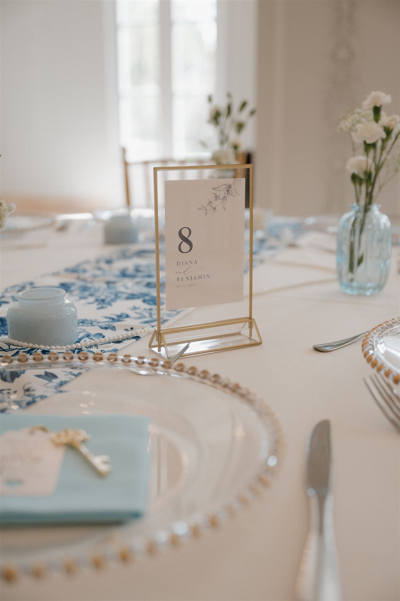 Wedding table detail with gold frame table number and blue accents on white linens.