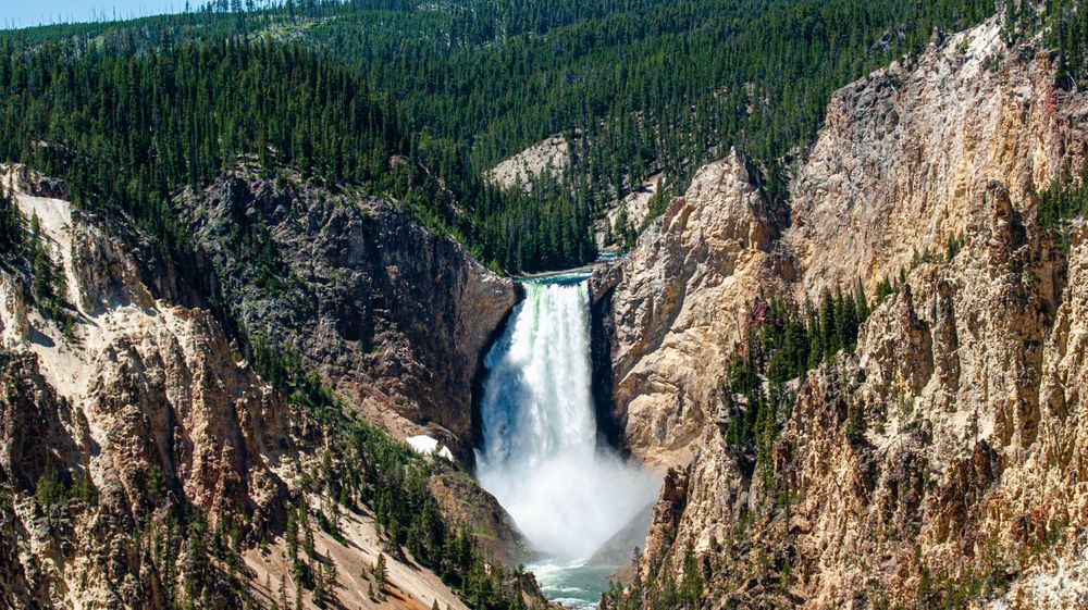 Wide angle view of a dramatic waterfall flowing through steep canyon walls in Yellowstone.