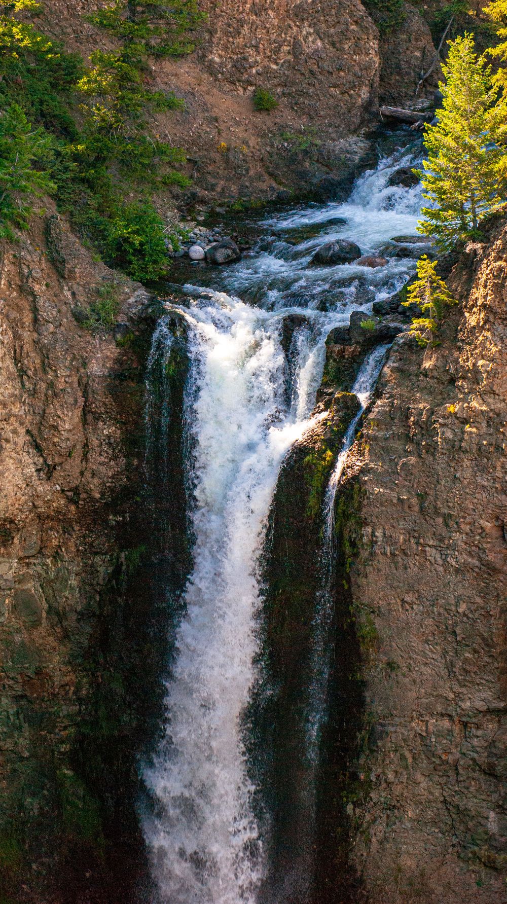 Powerful waterfall plunges down a rocky cliff face surrounded by dense forest vegetation.