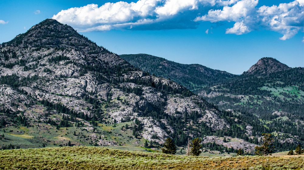 Panoramic mountain landscape under blue skies with white puffy clouds stretches across the horizon.
