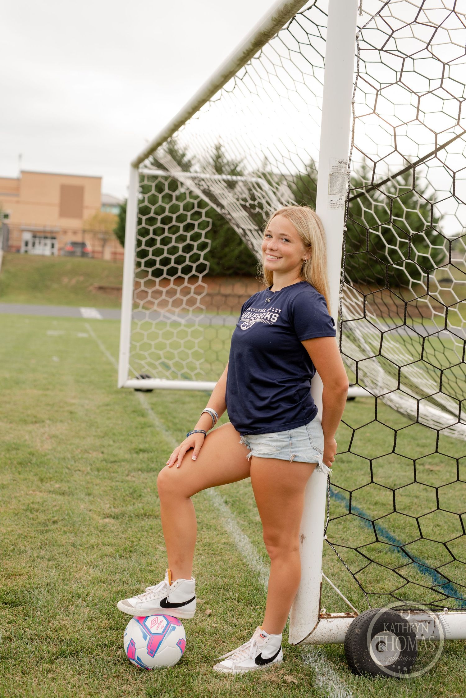 Soccer player posing with colorful ball by goal post wearing navy jersey.
