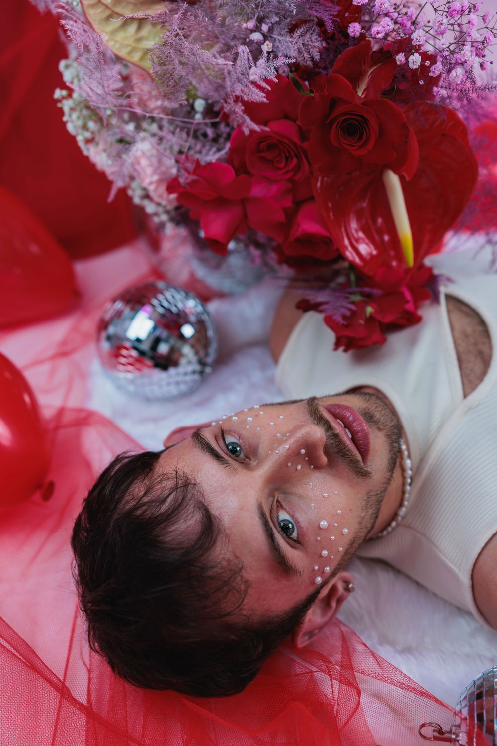 male model posing with pearls on his face amongst flowers and heart balloons for Valentine's shoot in Hove studio