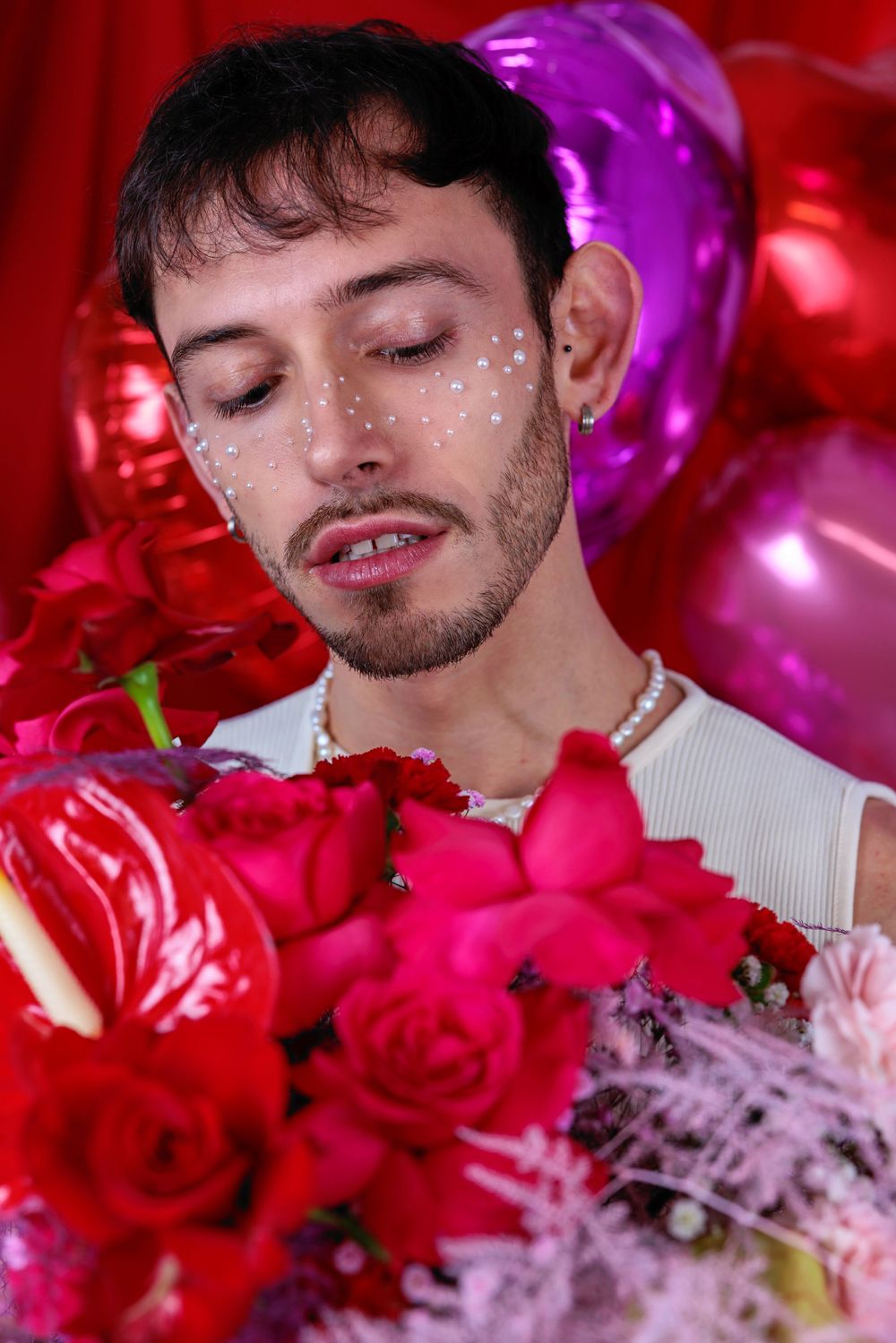 male model posing with pearls on his face amongst flowers and heart balloons for Valentine's shoot in Hove studio