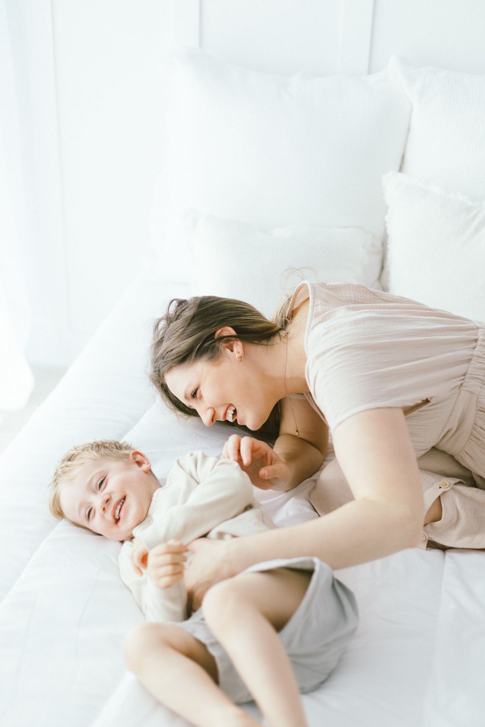 Parent and child sharing laughter while playing together on white bedding.