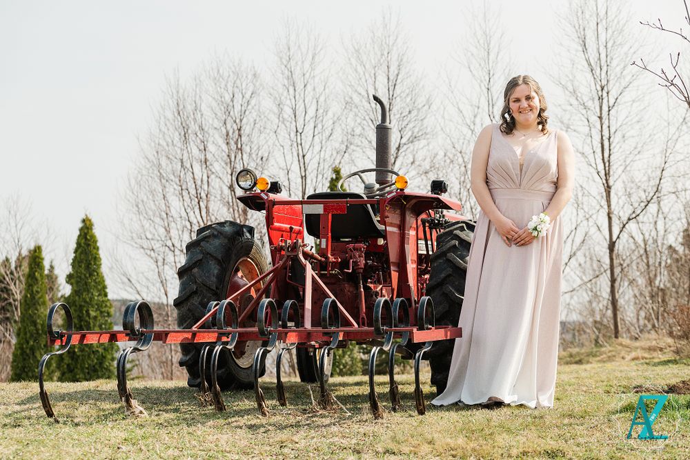Elegant long dress posed in front of vintage red farm tractor in rustic outdoor setting.