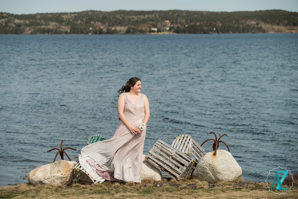 Woman in flowing dress poses on rocky shore with lobster traps and ocean view.