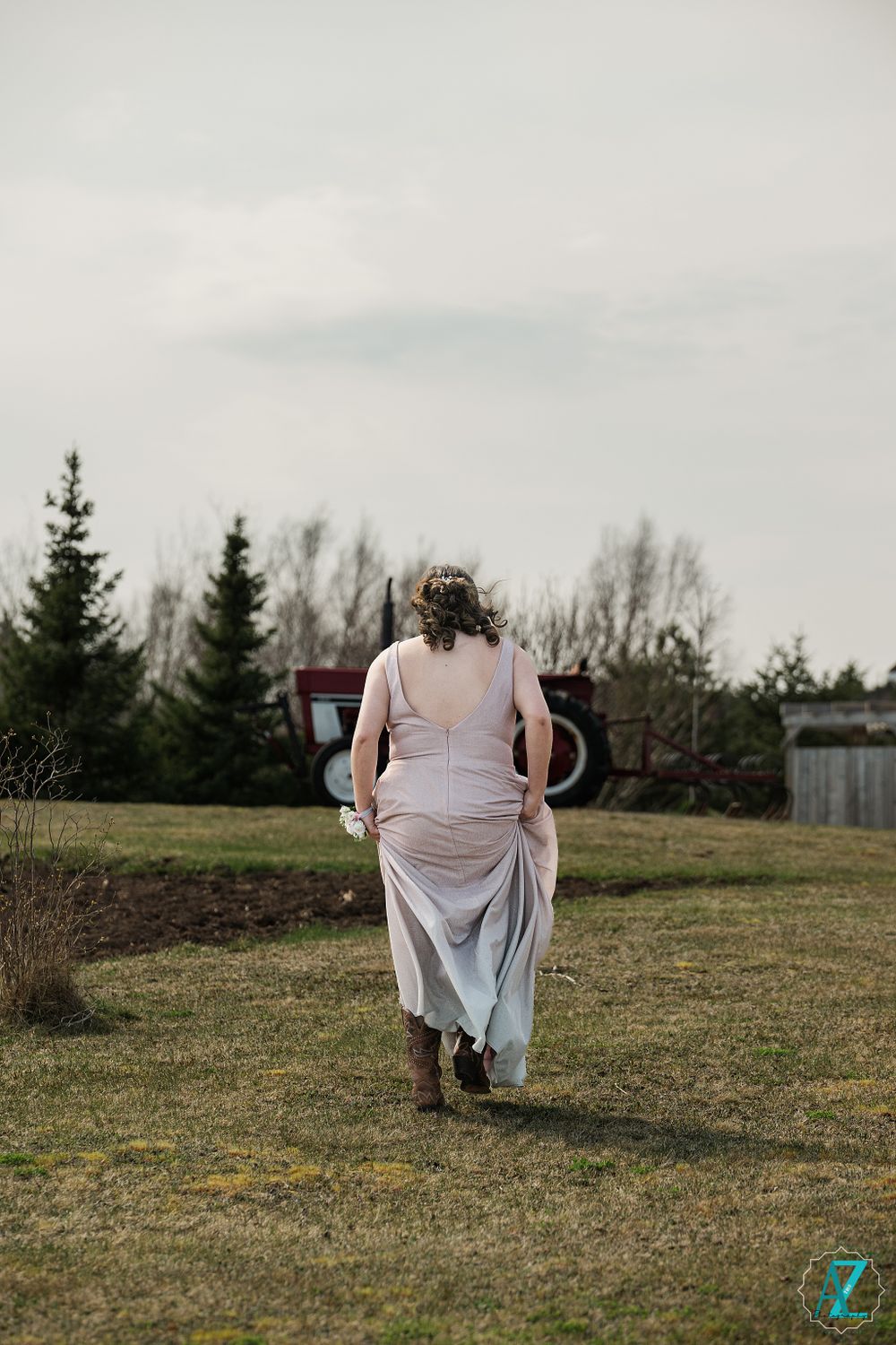 Back view of person in flowing dress walking across grassy field on overcast day.