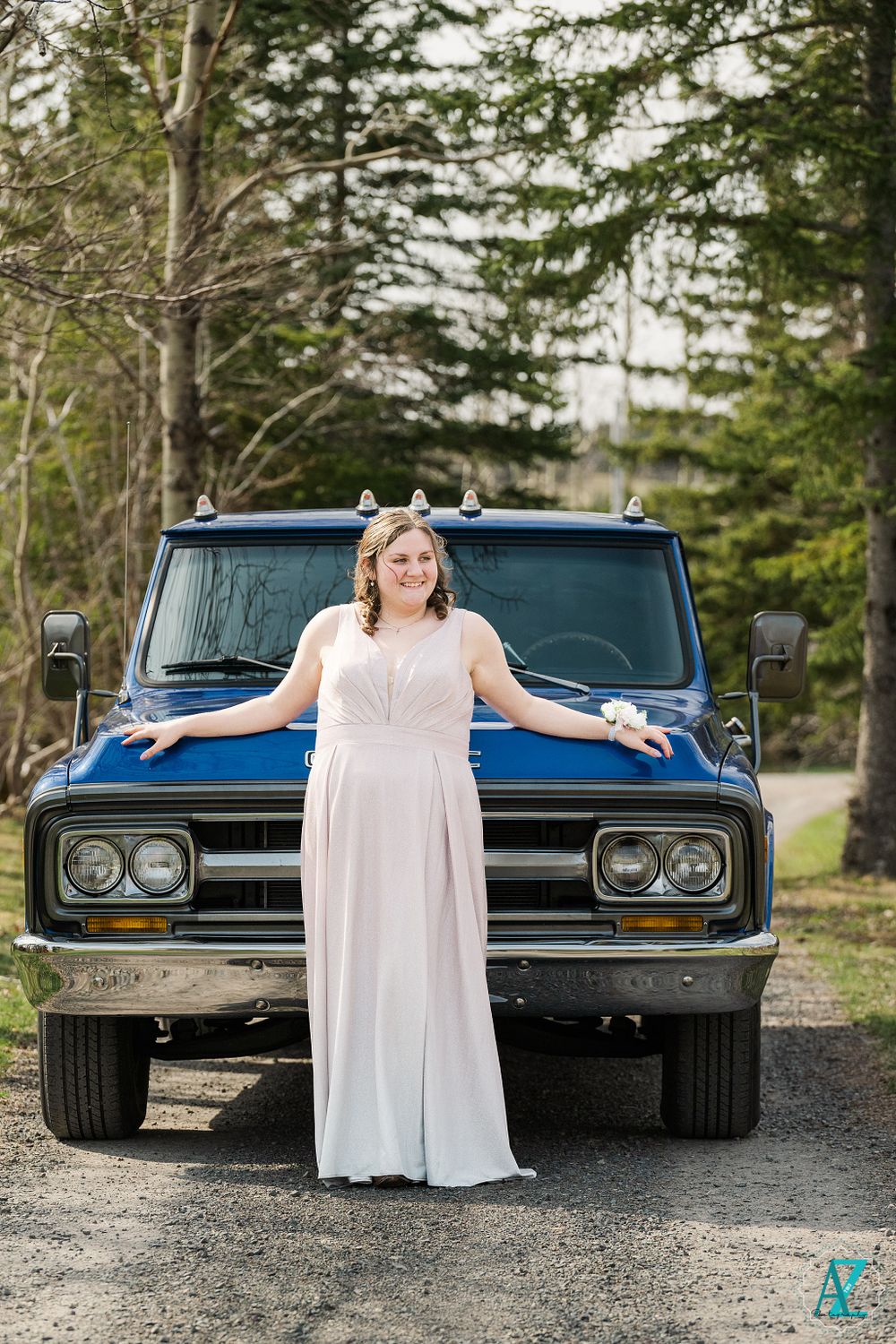 White long dress and vintage blue GMC truck against evergreen forest backdrop.