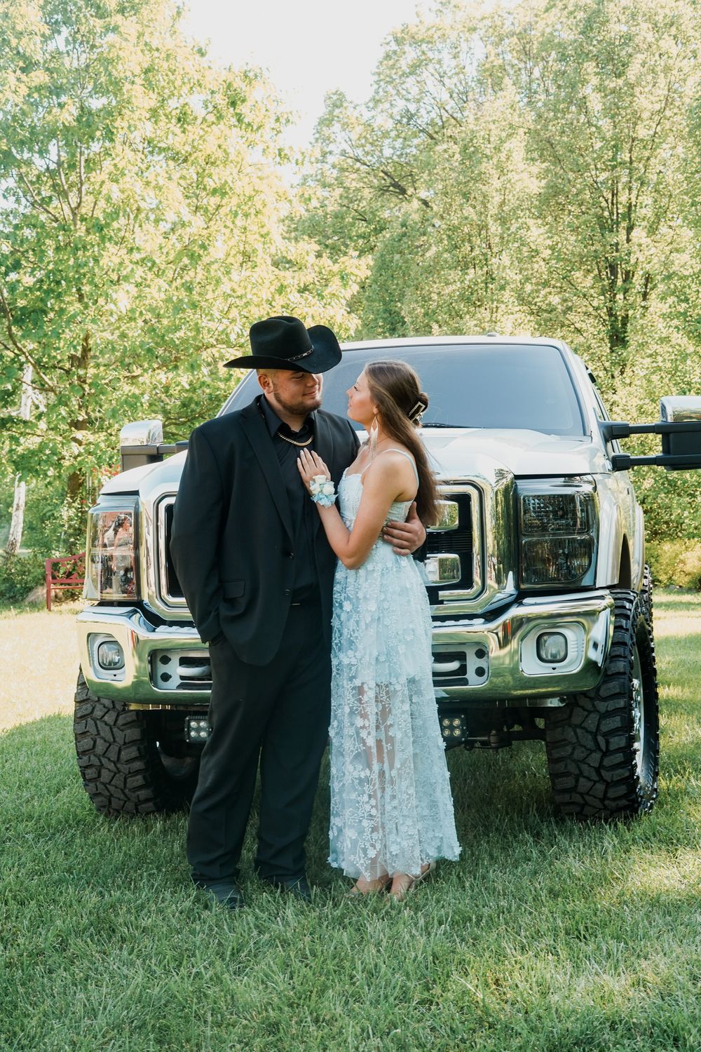 A couple embraces near trucks parked on grass during a sunny afternoon.