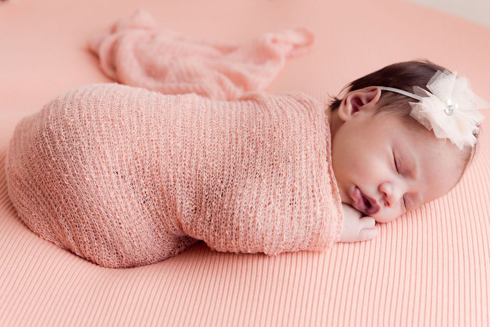 sleeping baby wrapped in peach coloured wrap and headband