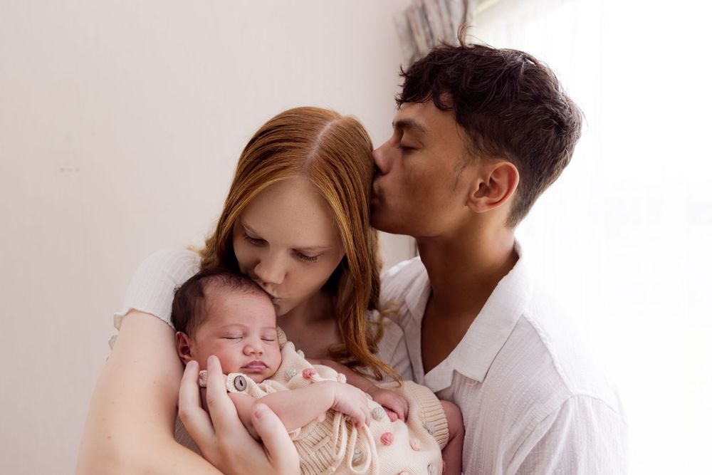 mum and dad holding baby and dad kissing mum on head