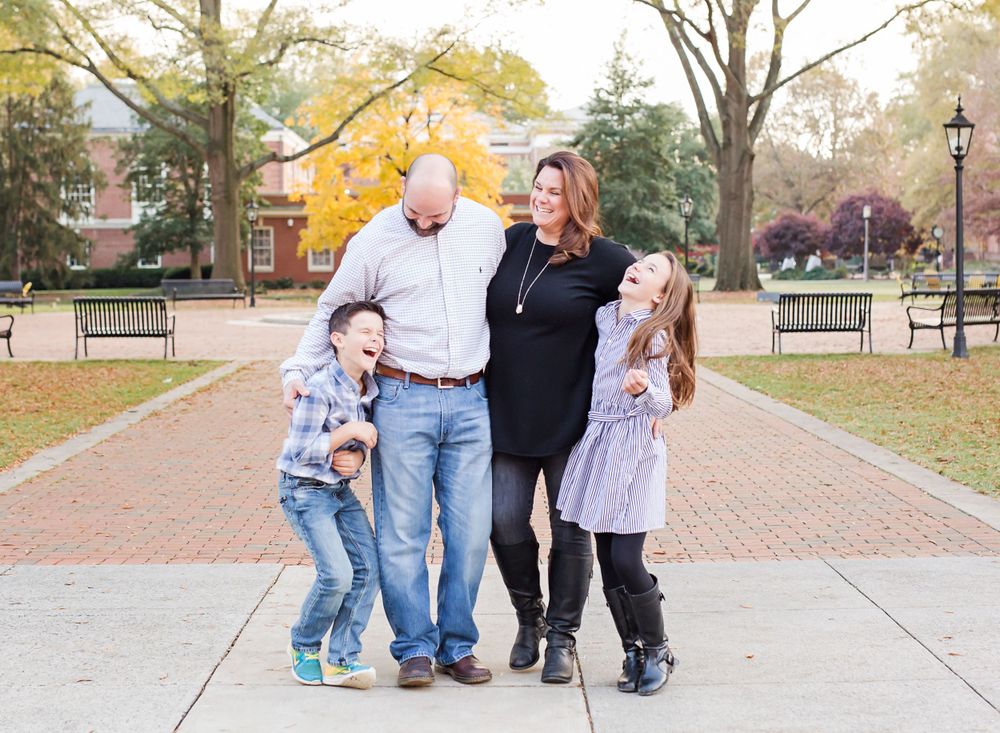 A happy family of four poses together on brick pathway during autumn.