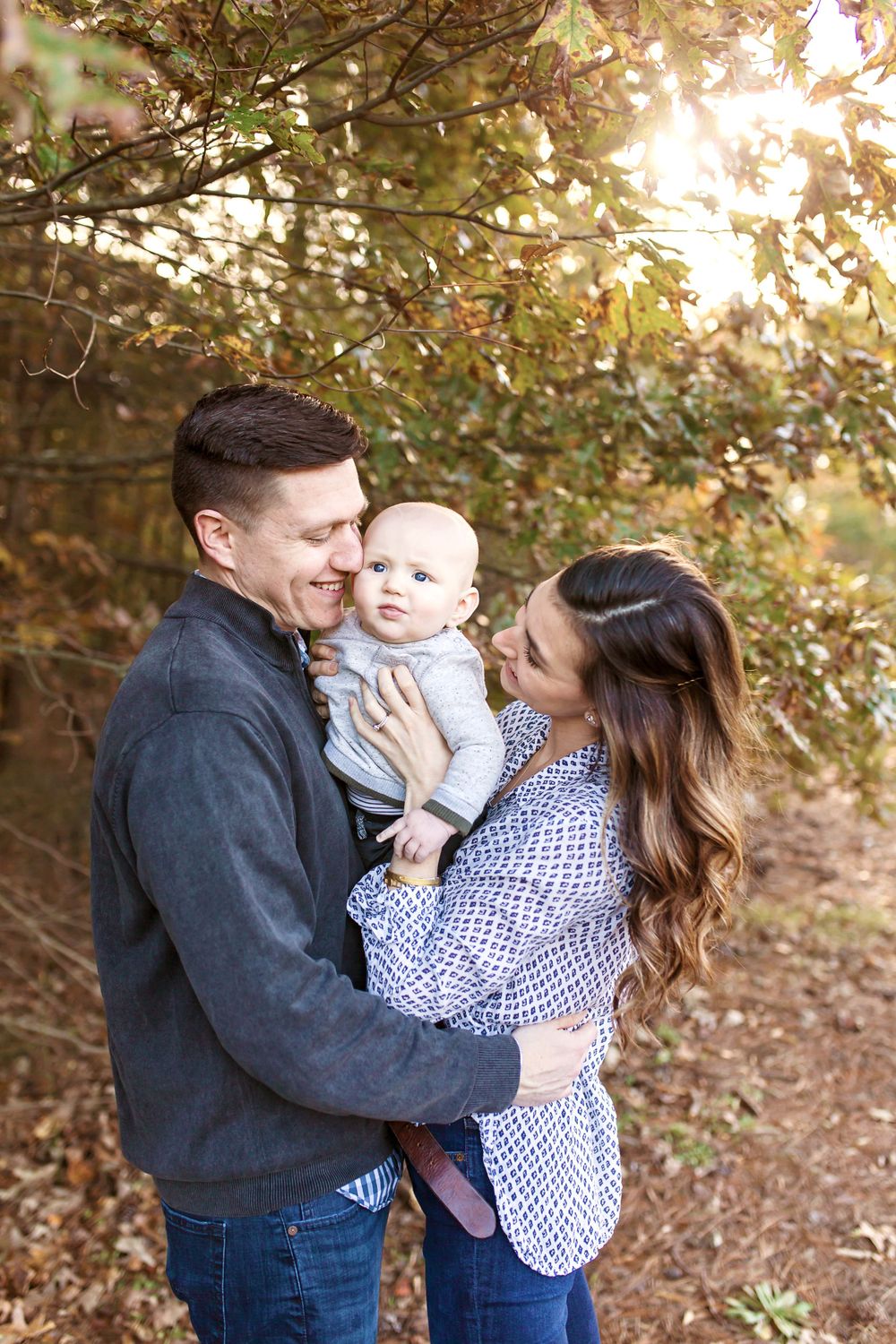 A young family shares tender moment together under tree branches.