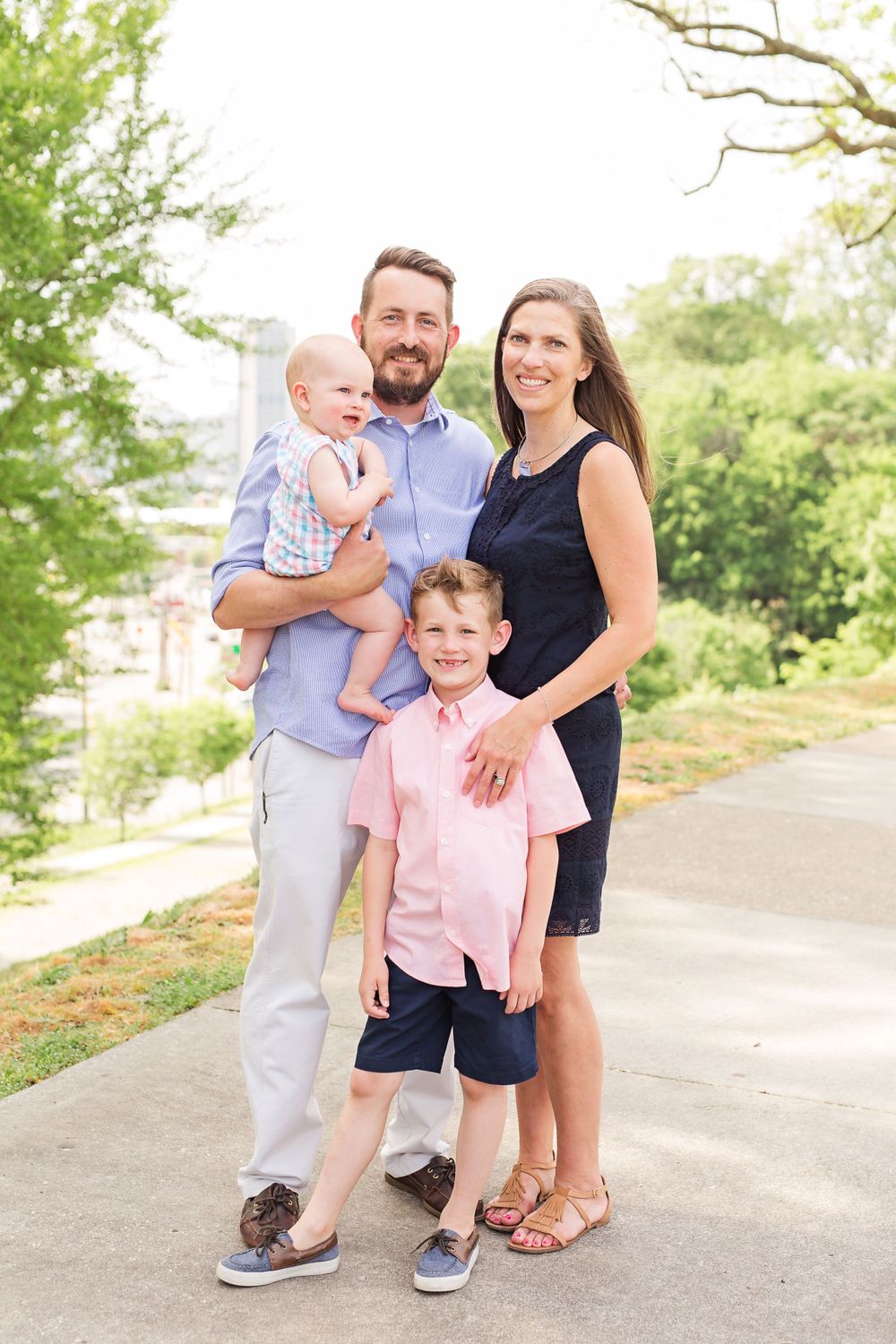 Family of four poses together outdoors in coordinating blue and pink casual attire.