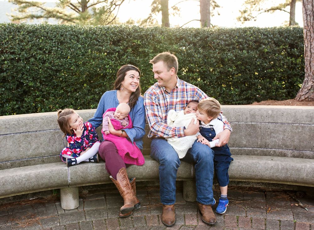 Family sits together on curved stone bench during outdoor photo session.