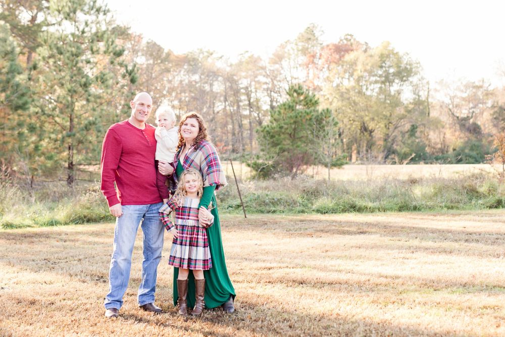 A family stands together in an open field during fall season.
