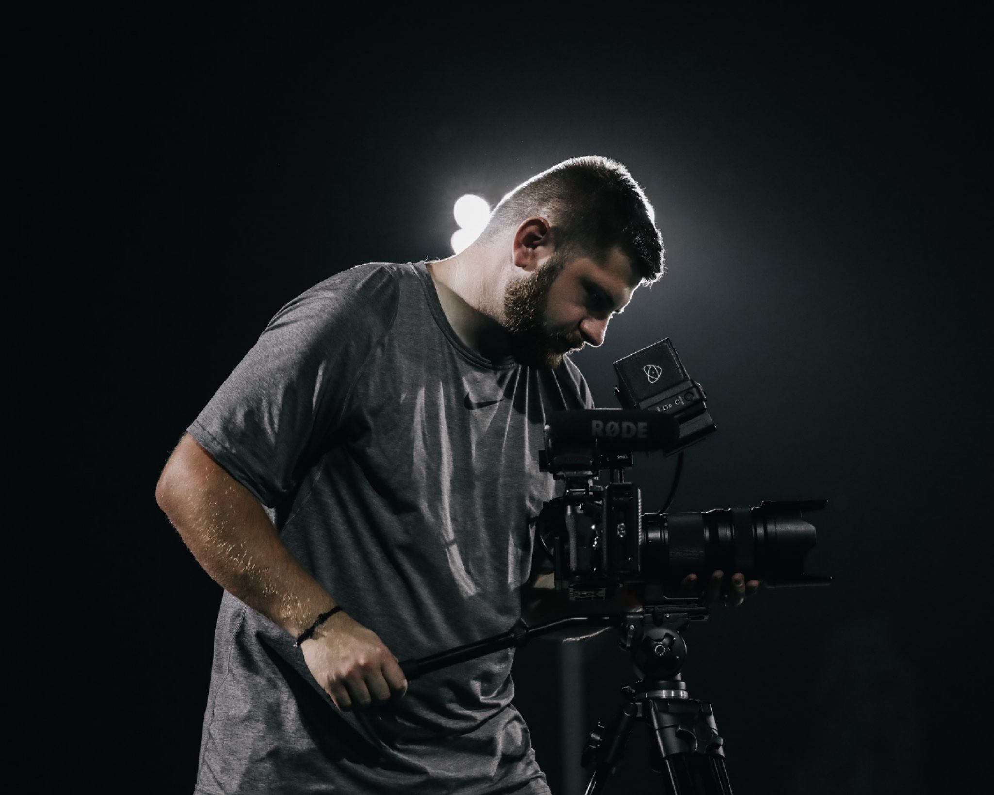 Cinematographer operating a professional video camera in dramatic lighting with backlit silhouette.