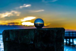 Crystal ball captures a vibrant sunset over a pier silhouetted against an orange sky.