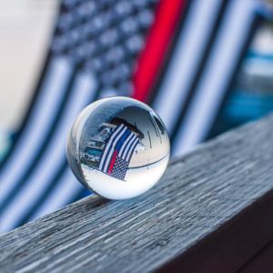 Glass sphere reflects American flag stripes on weathered wooden surface.
