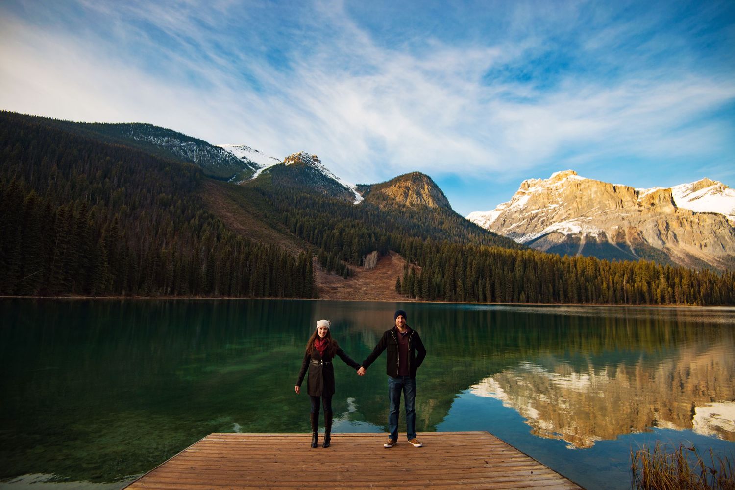 Lana and Adam engagement photo on a dock by Emerald Lake. Mountains in the distance.
