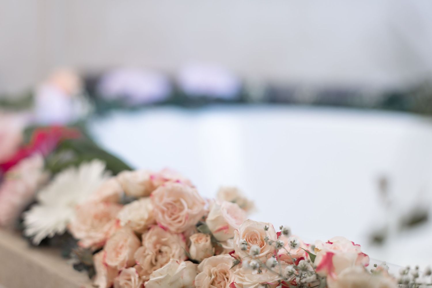 Delicate arrangement of pink roses and baby's breath along white bathtub edge.