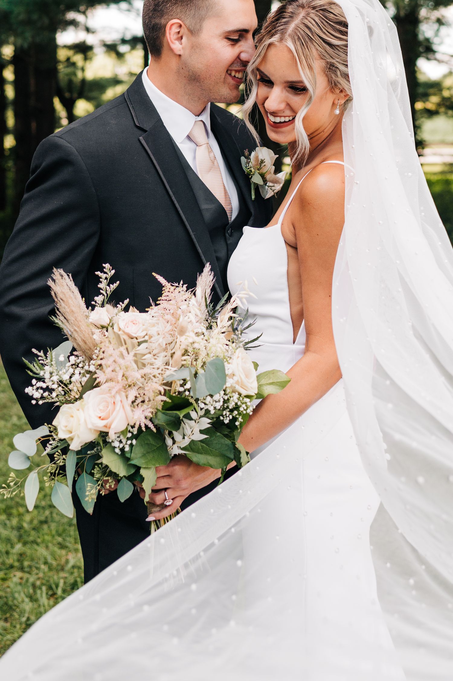 Wedding photo featuring elegant bridal gown and delicate bouquet with pampas grass and greenery.