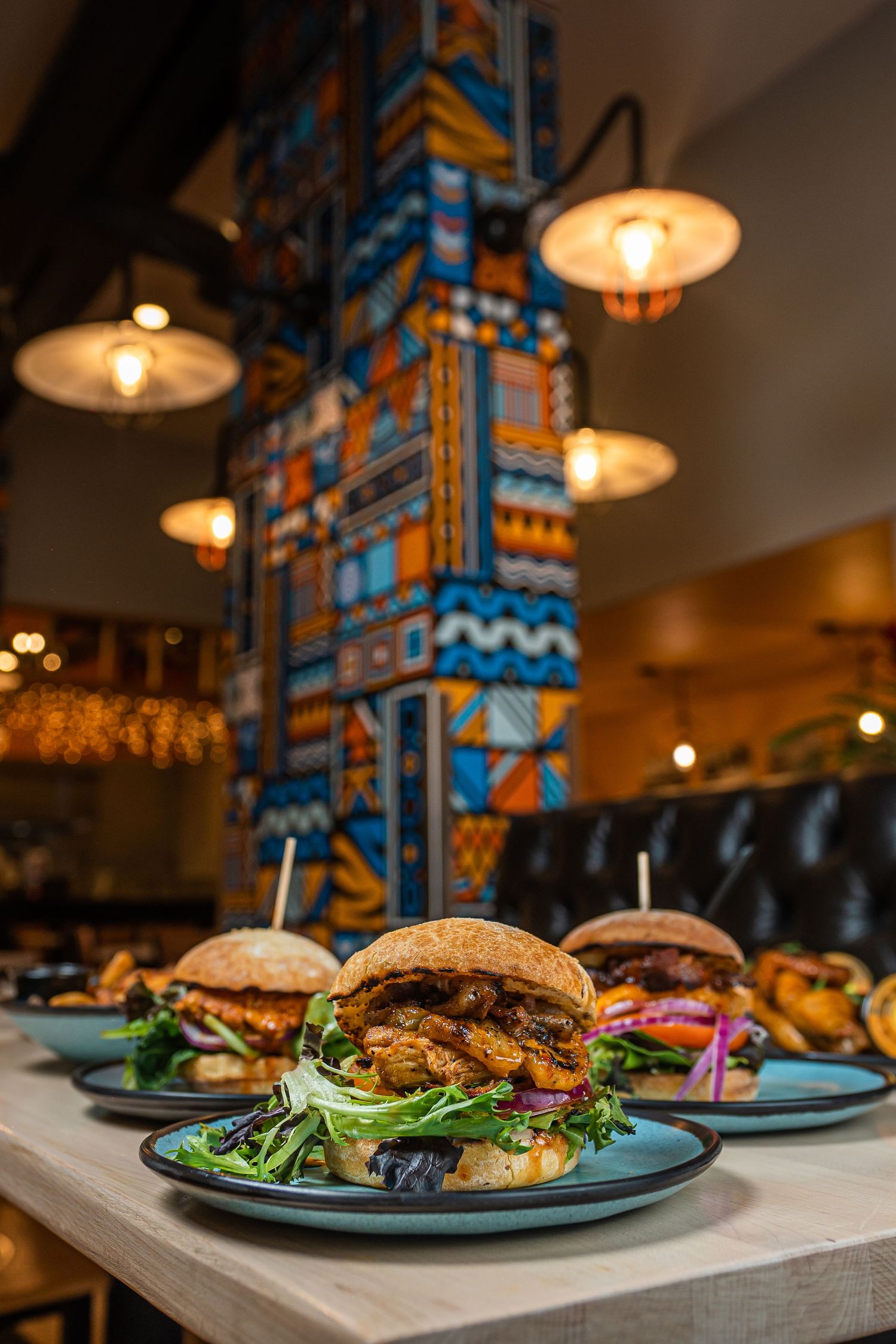 Gourmet burgers on blue plates displayed in row at vibrant restaurant with colorful decor.