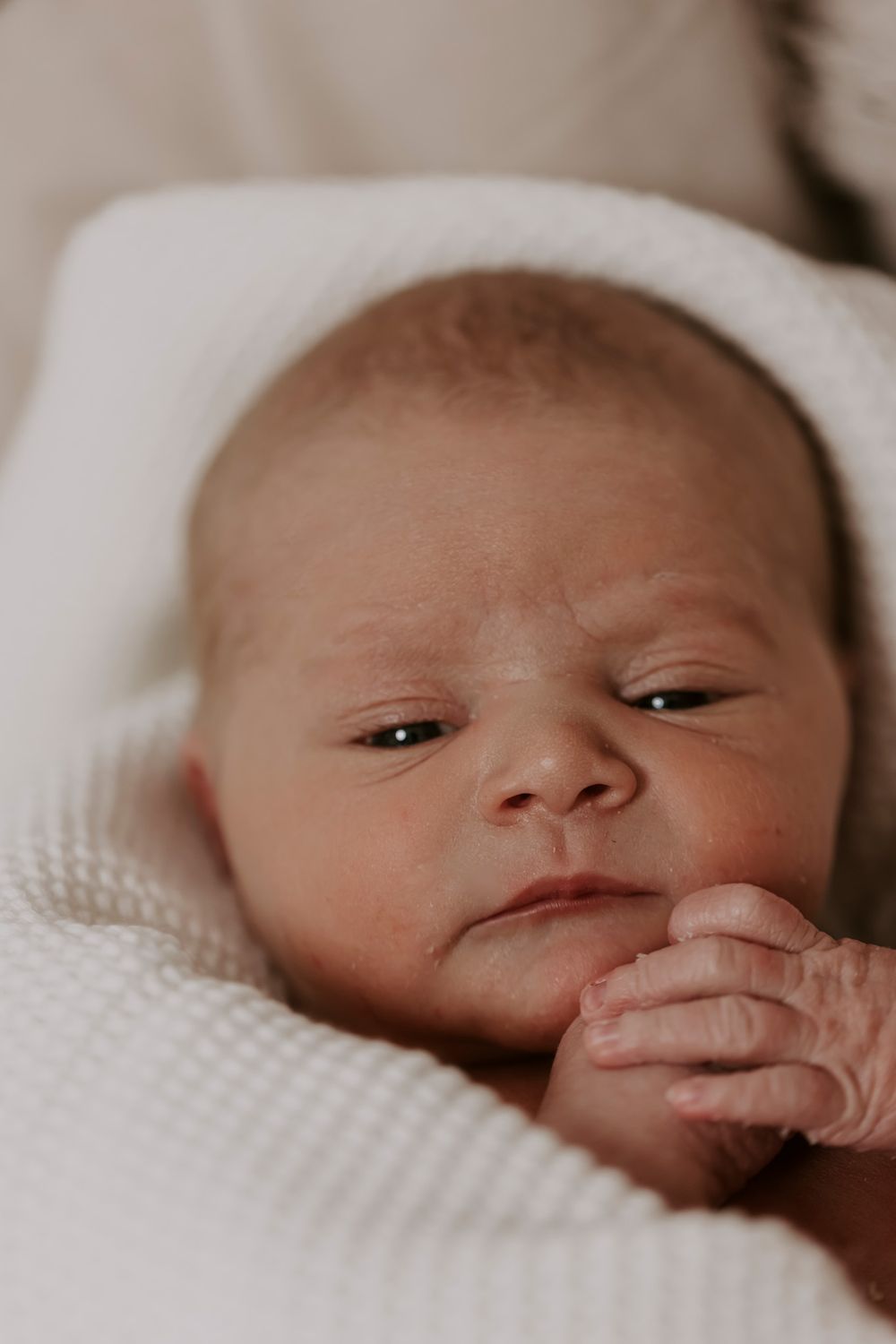 Nærbilledeportræt af en nyfødt baby med let åbne øjne på et hvidt tekstureret tæppe.