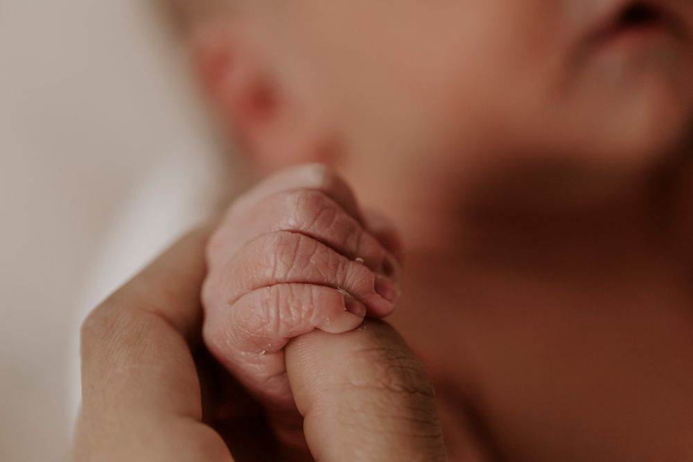 Blide hænder holder en nyfødt babys fødder i varmt lys.