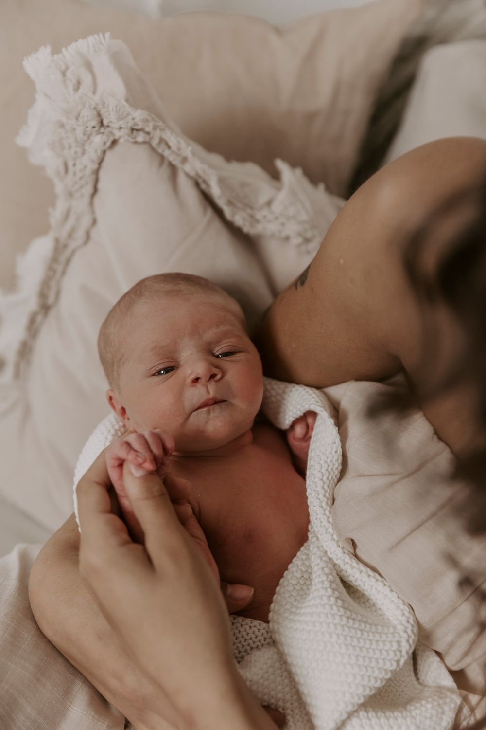 Nyfødt baby svøbt i et hvidt strikket tæppe, mens den holdes i armene.