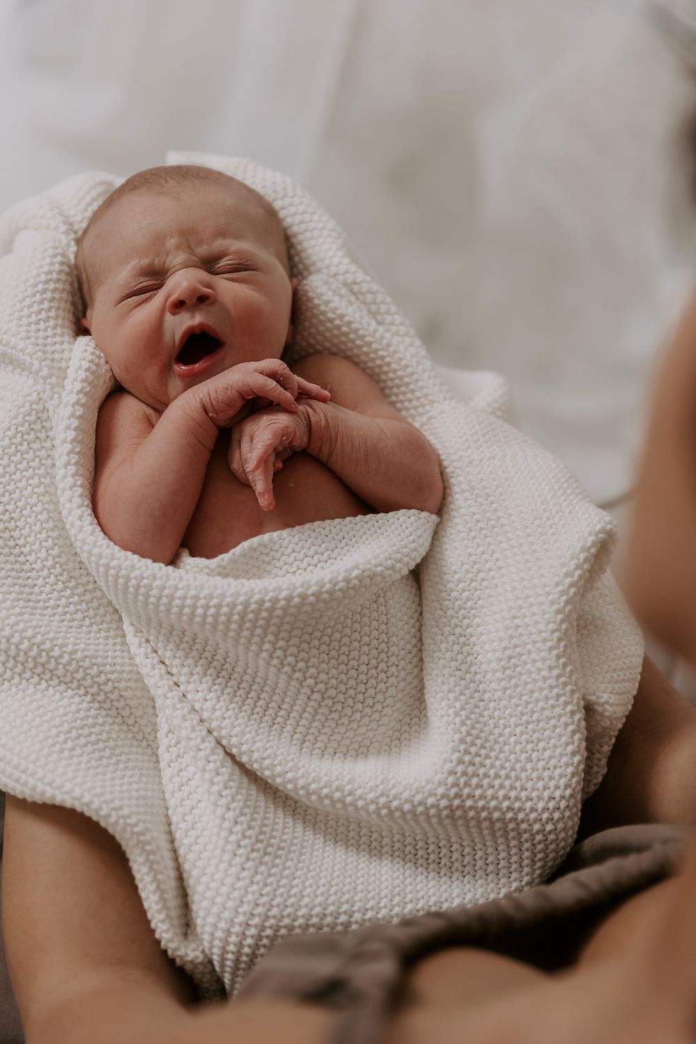 Nyfødt baby gaber, mens den er svøbt i et hvidt strikket tæppe.