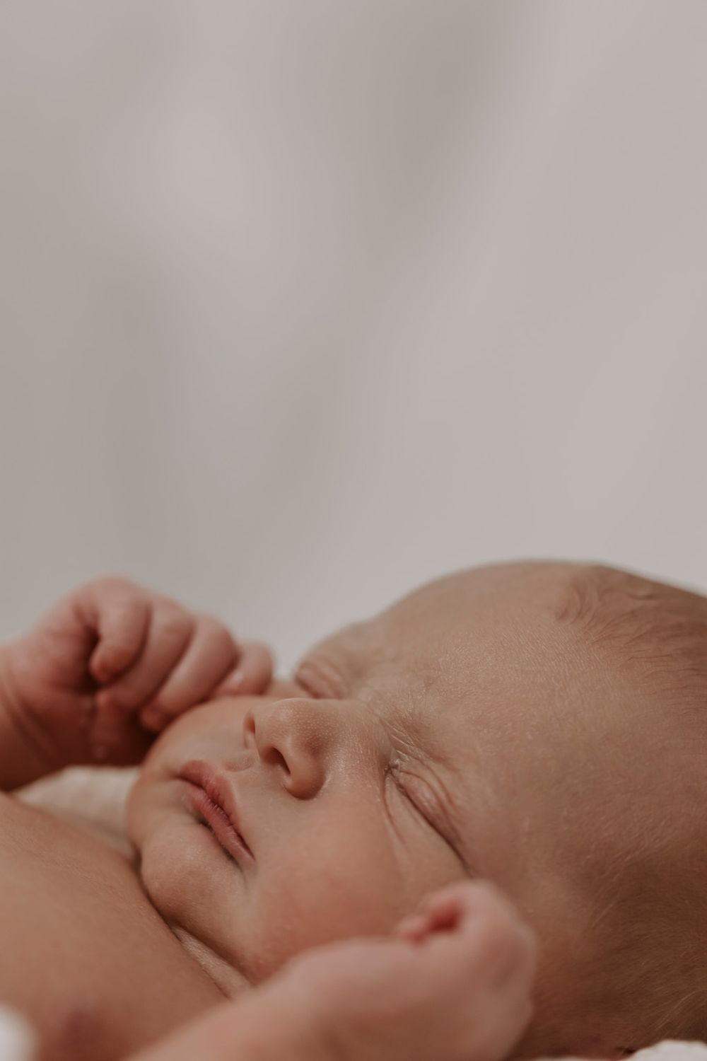 Sideprofil af sovende baby med fine ansigtstræk mod en minimalistisk baggrund.