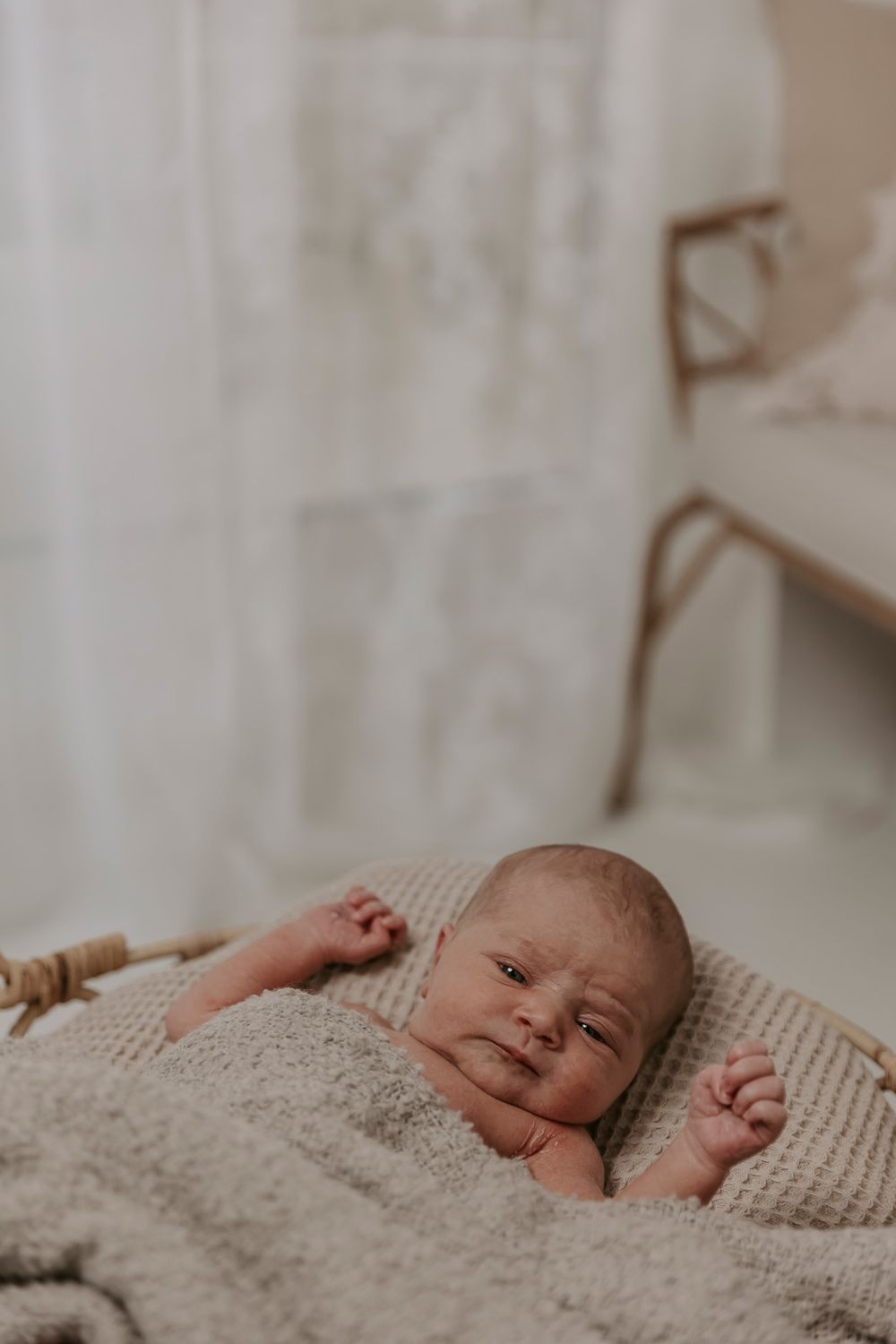 Nyfødt baby ligger på siden under et hyggeligt beige tæppe i naturligt lys.