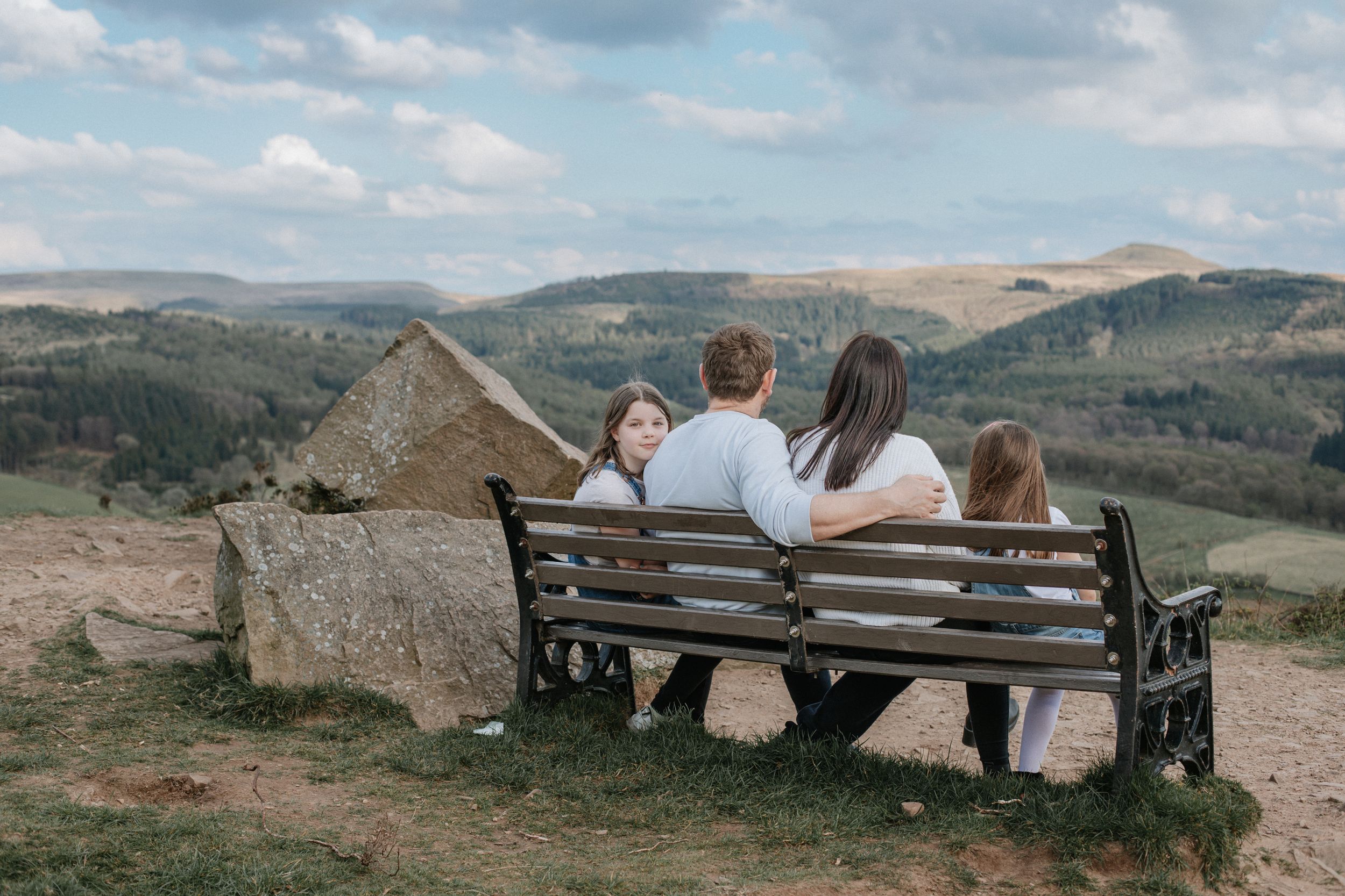 Group sitting on wooden bench overlooking scenic mountain landscape.