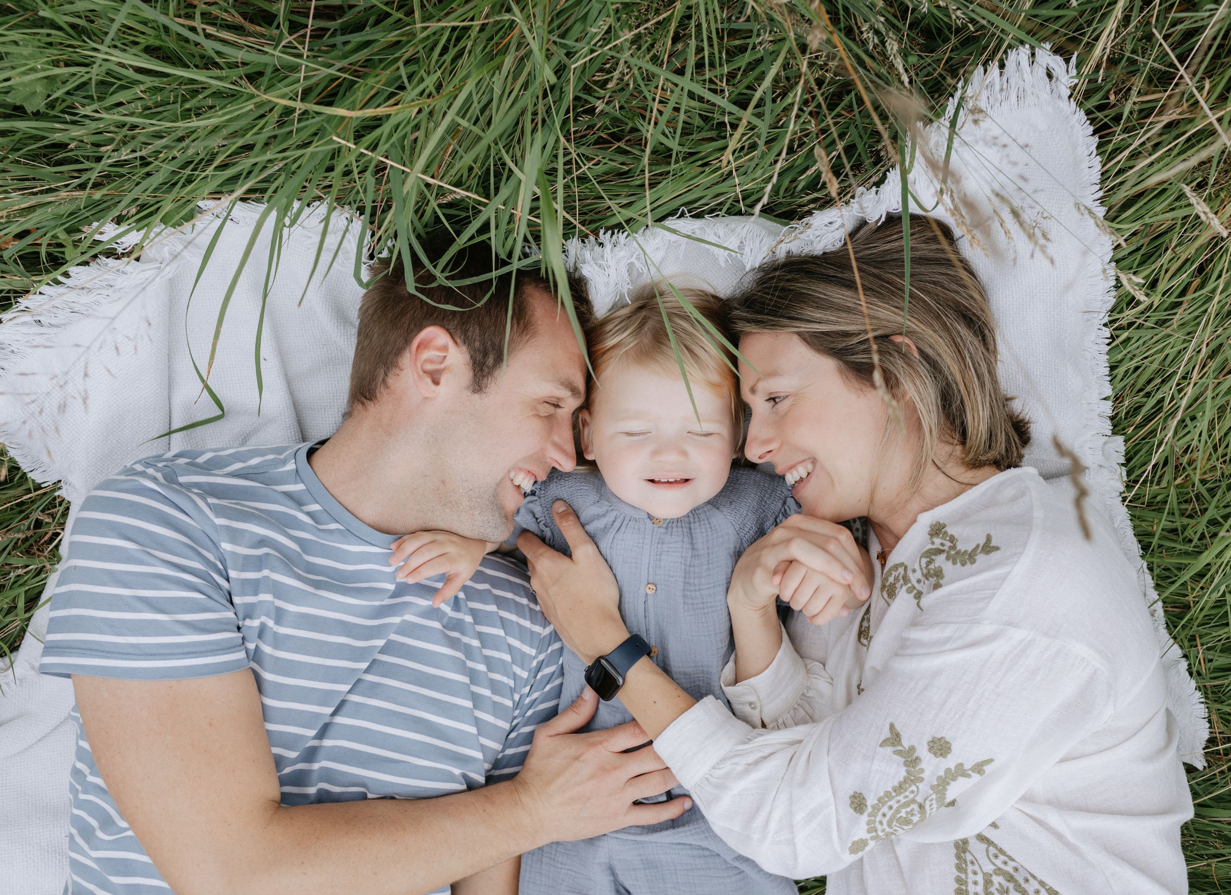 A loving family moment captured in a series of tender photos laying in green grass together.