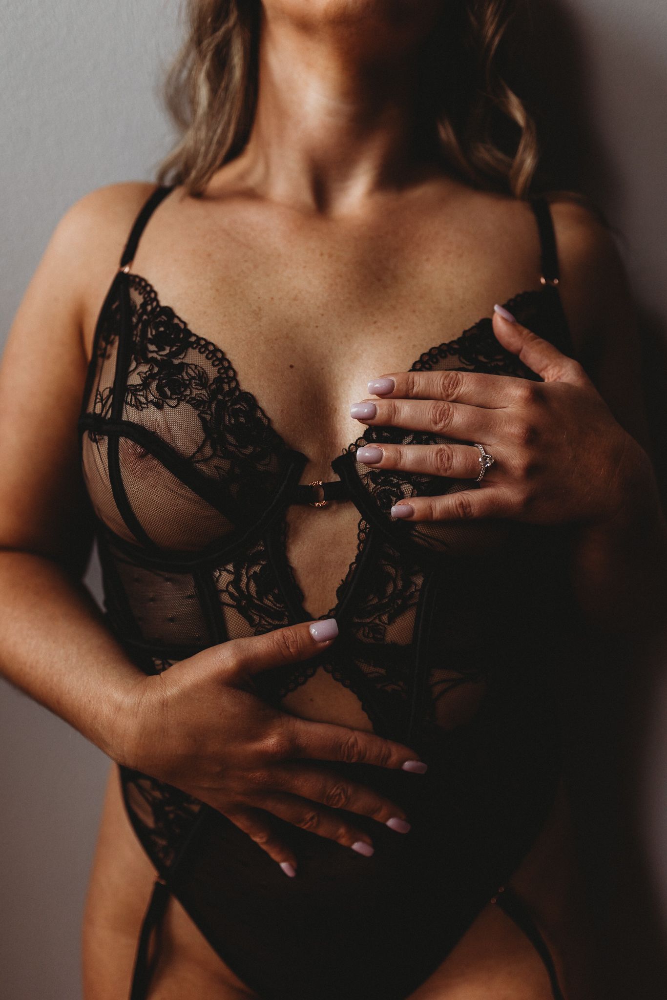 Close-up view of black lace lingerie bodysuit details with manicured hands.