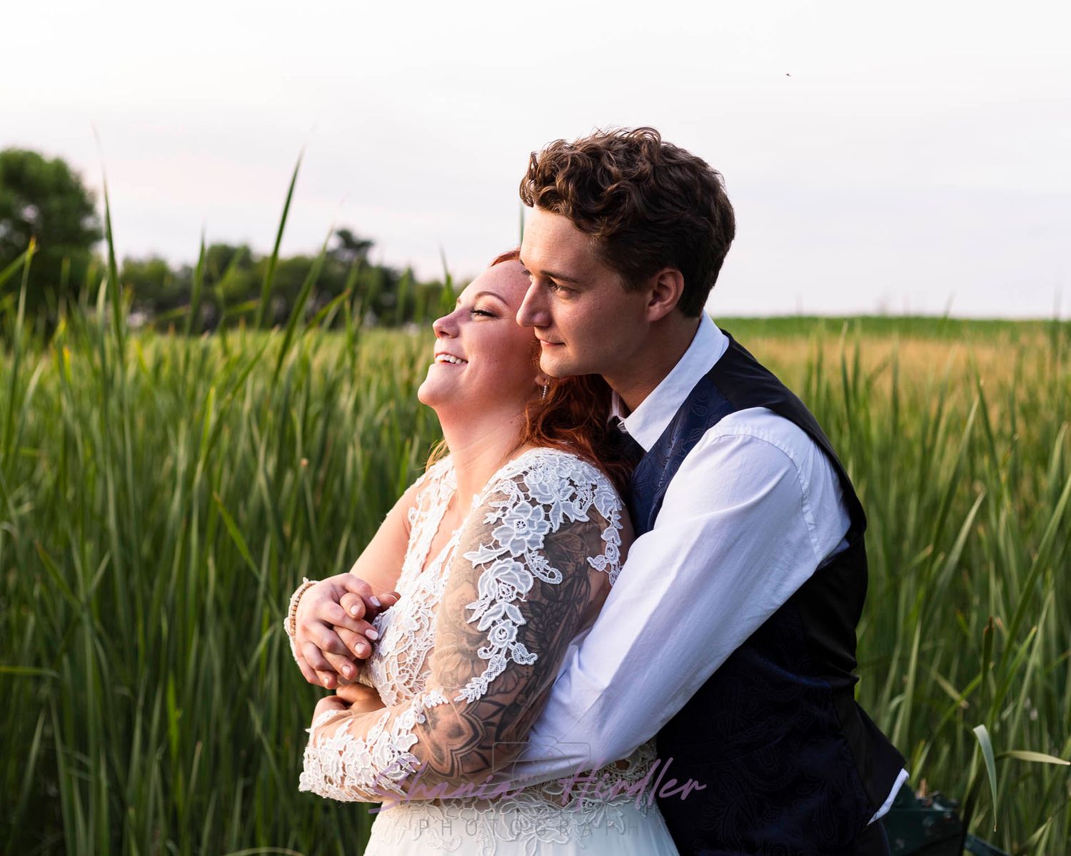 A Groom holds his bride as they look into the sunset over a reedy pond at the Pondview Wedding Venue in Central, MN