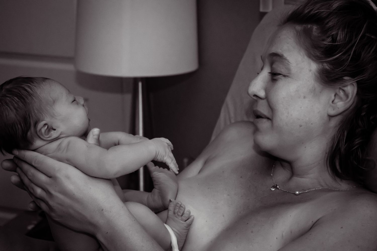 Black and white image of a mother holding up her newborn baby and smiling.
