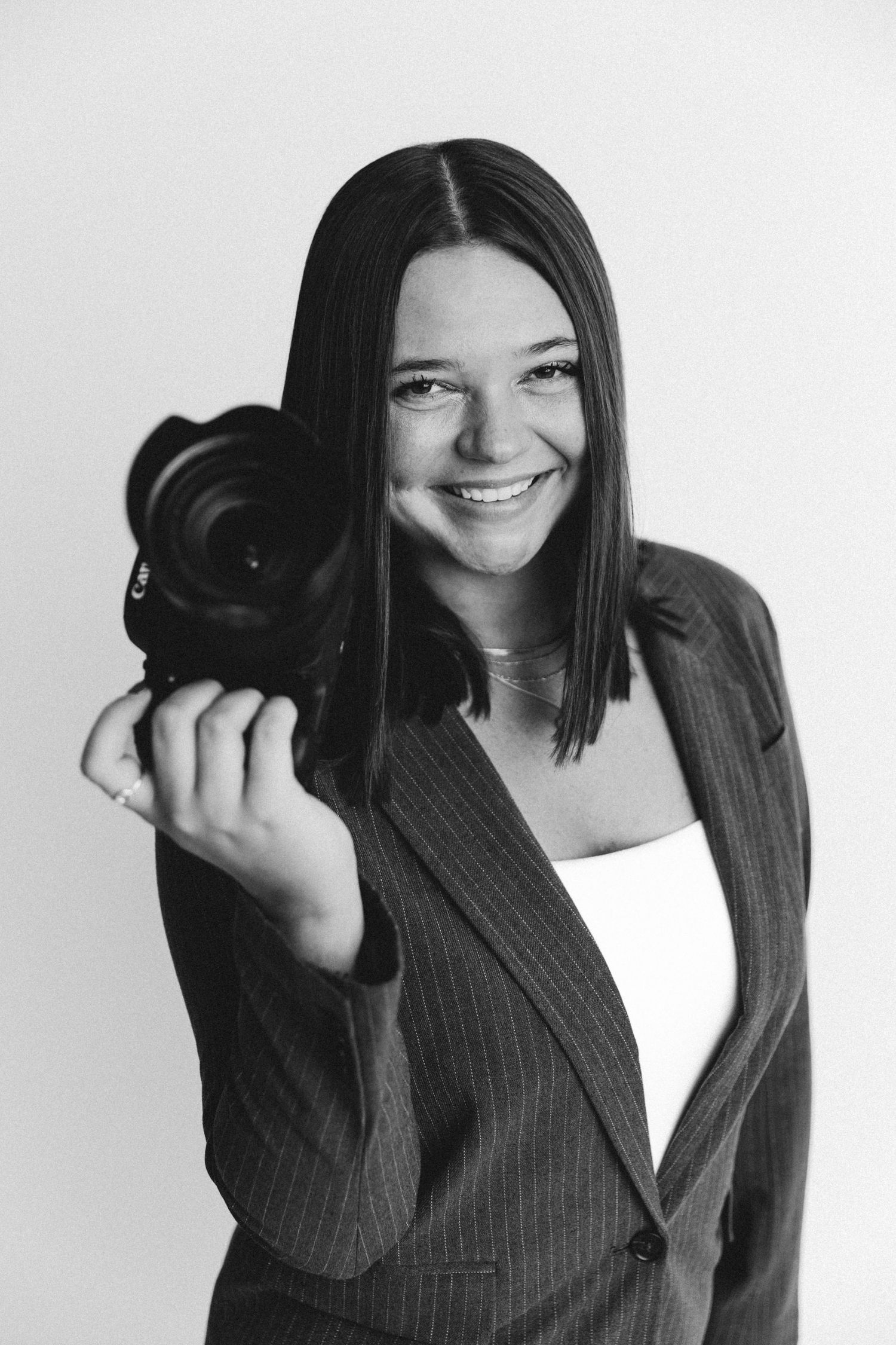 Professional photographer in business attire holding DSLR camera against white background.