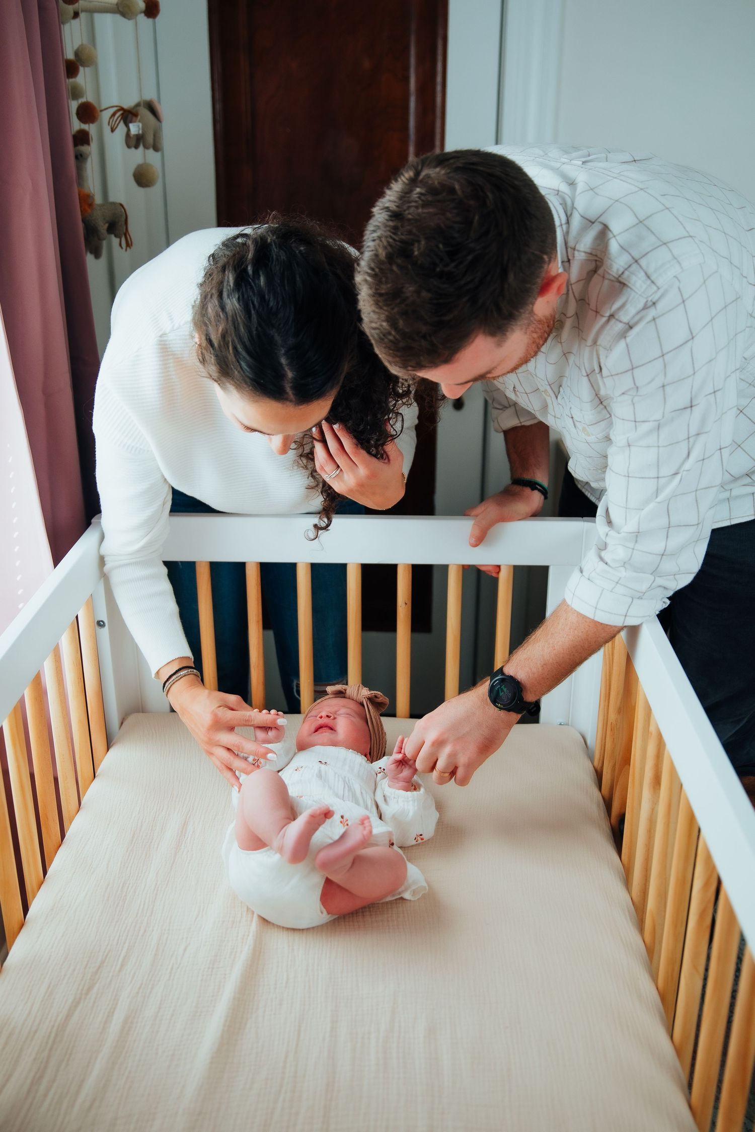 Parents leaning over wooden crib looking at baby. in-home newborn photoshoot