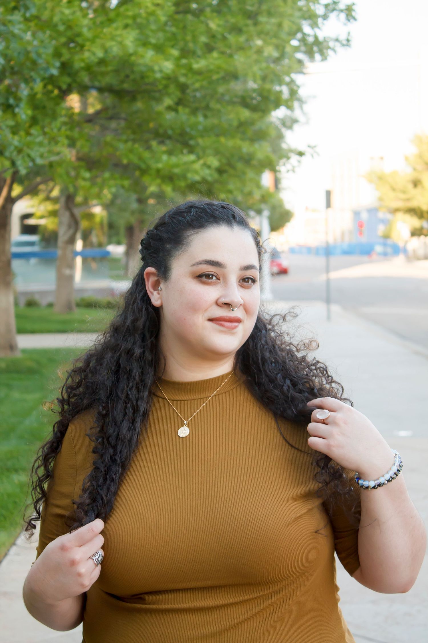 Outdoor portrait of someone in a mustard top playing with their long curly hair.