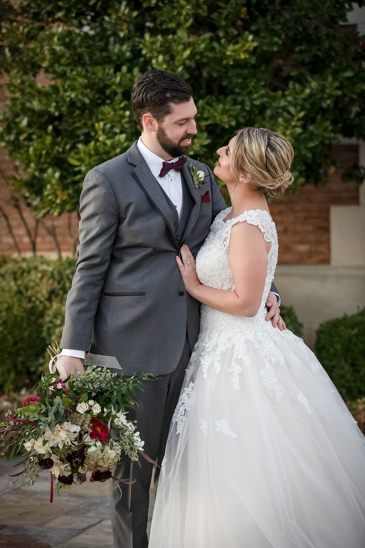 bride in grey suit looking & hold bride close for spring texas wedding at grapevine vineyard