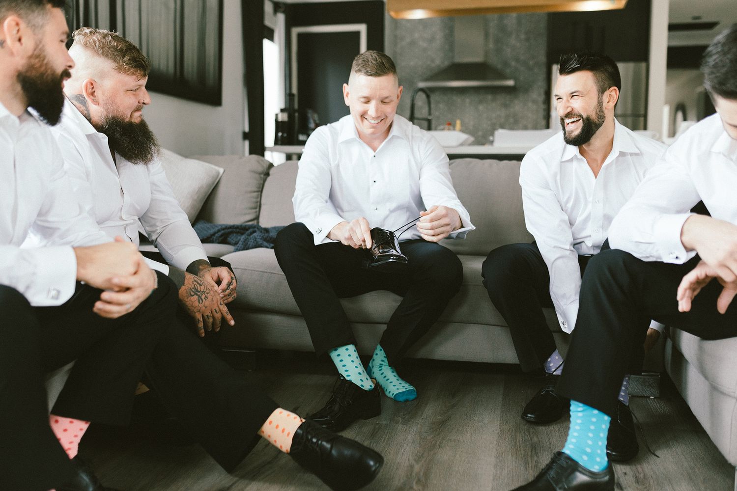 Friends relaxing on a grey couch showing off their colorful socks during a formal event.