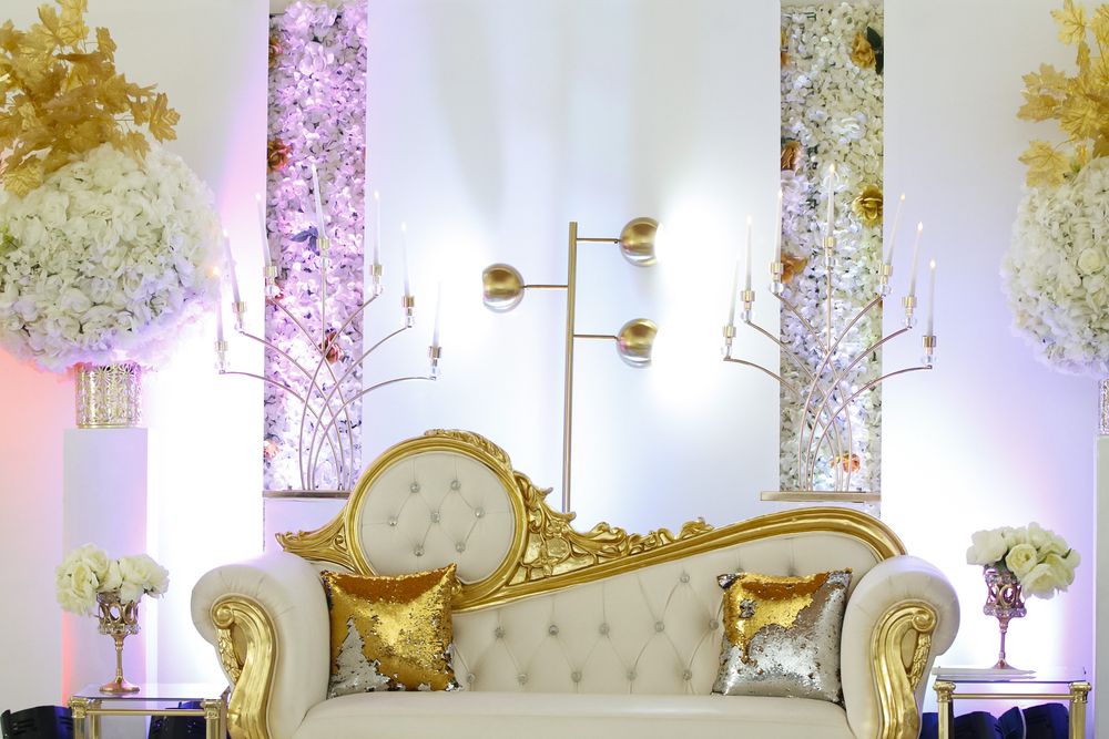 Elegant white and gold wedding reception venue with tufted chairs and floral arrangements.